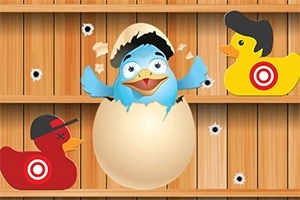 Chú chim xanh đội mũ lưỡi trai nở ra từ quả trứng giữa hai con vịt đồ chơi màu đỏ và vàng, trên nền gỗ có lỗ đạn