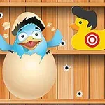 Chú chim xanh đội mũ lưỡi trai nở ra từ quả trứng giữa hai con vịt đồ chơi màu đỏ và vàng, trên nền gỗ có lỗ đạn